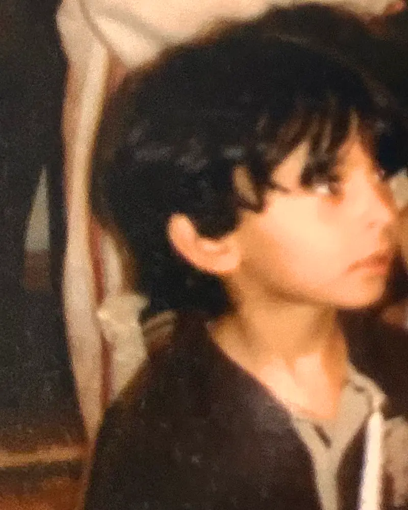 Old family photo of Mohammed as a small boy holding a white candle, looking intently at something out of frame.